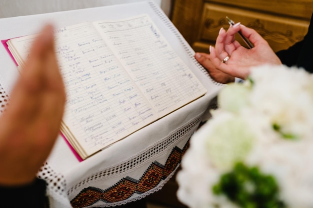 Стильная счастливая невеста держит ручку в руке и пишет да в журнале браков. Начало церемонии. Свадебное утро. Закройте вверх. Место для текста.