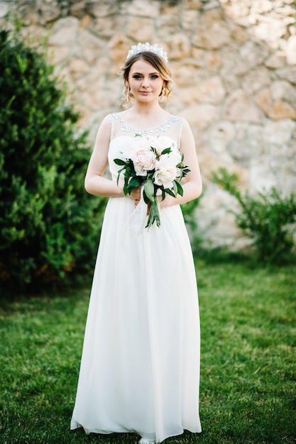 Stylish happy bride with bouquet of peonies with crown.