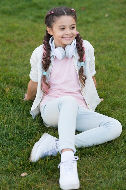 stylish happy child relax on green grass little girl listen music spring mood mp3 player happy little girl audio book happy kid in headphones happy childhood little girl having fun pure joy
