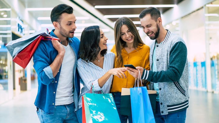 Photo stylish happy excited friends with shopping bags are looking together on the smart phone and chatting about sales in the mall