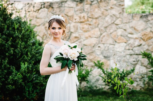 Stylish happy smile bride with bouquet of peonies with crown