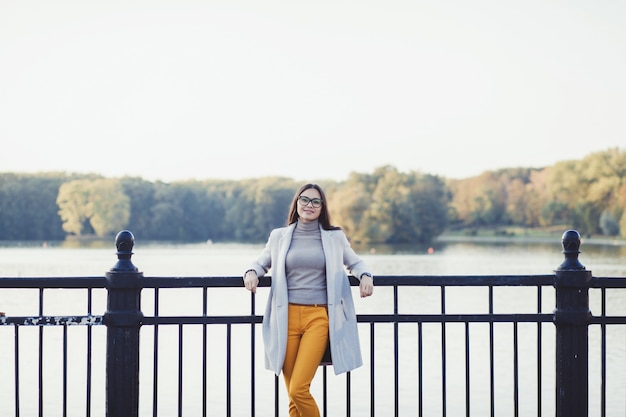 Stylish happy woman in autumn coat of the river in the park