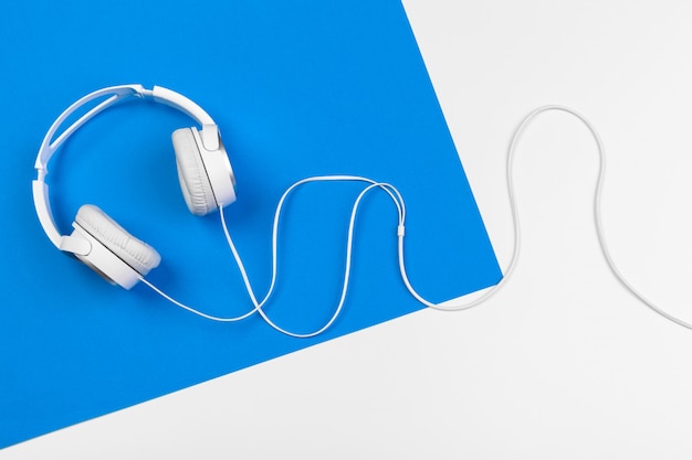 Stylish headphones on blue and white color background, top view.