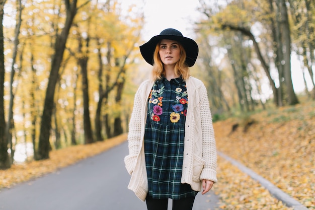 Stylish hippie girl in a knitted sweater and hat walks in the autumn park.