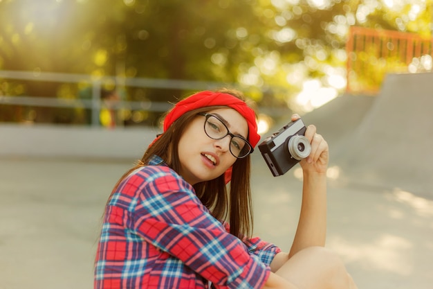 Stylish hipster girl holding retro camera in hands on a bright sunny day. Youth concept