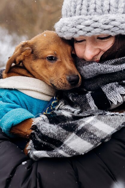 Foto elegante ragazza hipster che abbraccia e accarezza un simpatico cucciolo nel freddo inverno nevoso del parco momenti di vero concetto di adozione della felicità salva gli animali
