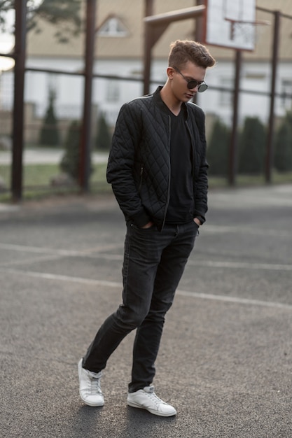 Premium Photo | Stylish hipster man in black trendy clothes with white shoes  poses at outdoor stadium