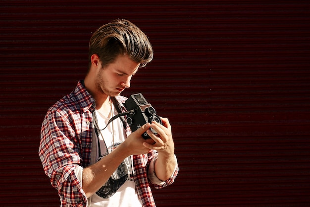 Stylish hipster man holding old retro analog photo camera on background of red garage door