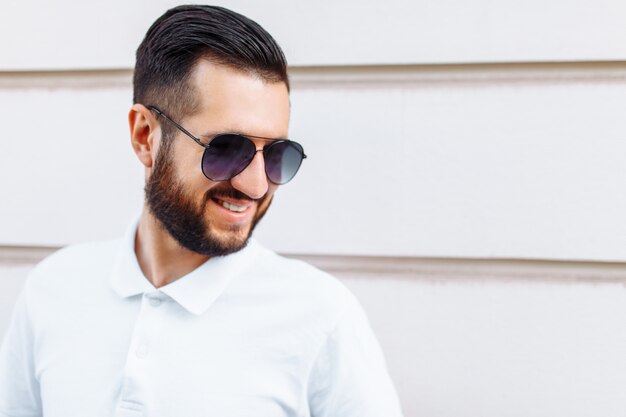 Photo stylish hipster in a white t-shirt and with a beard, standing near a white wooden wall