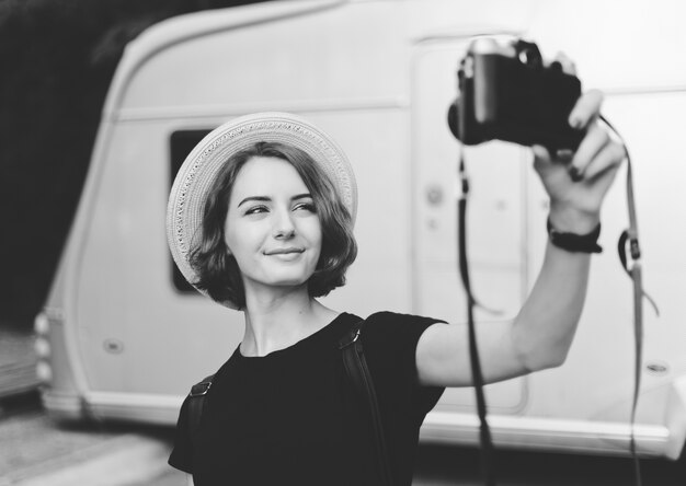 Stylish hipster woman in hat makes selfie portrait using retro camera. Black and white photo
