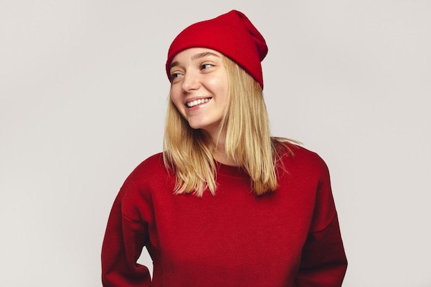 Foto elegante donna hipster che indossa un elegante cappello rosso e una felpa che sorride a