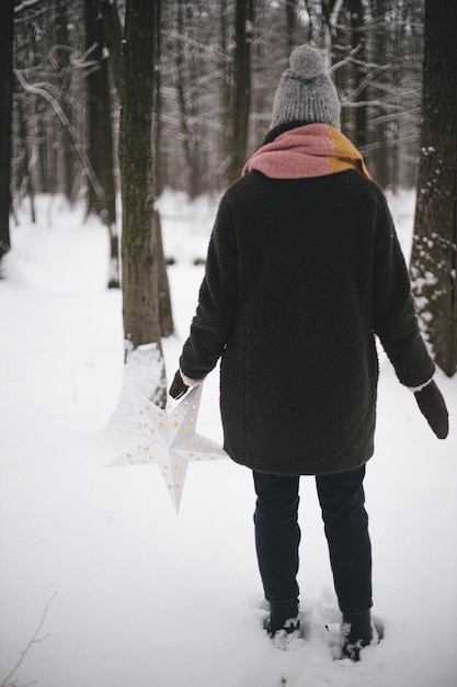 Stylish hipster woman with big white christmas star walking in\
snowy winter woods magic winter
