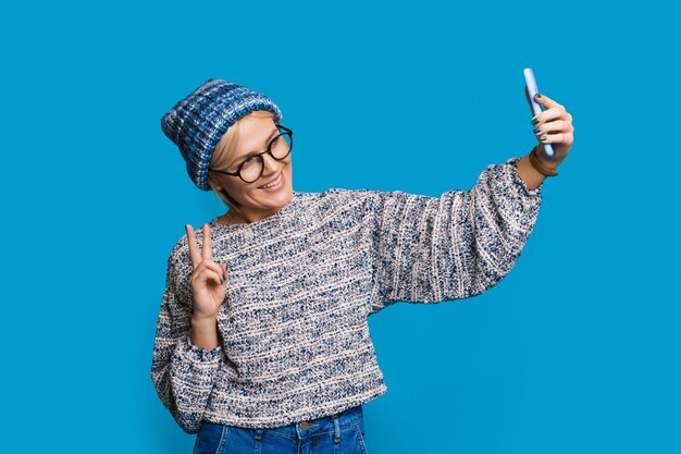 Immagine elegante con una donna con un cappello lavorato a maglia che fa un gesto di pace per selfie alla moda