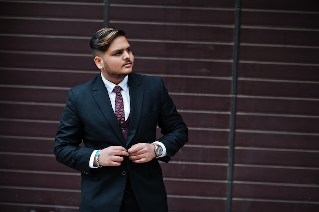 Stylish indian businessman in formal wear standing against brown shutter.