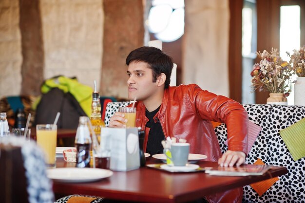 Elegante uomo indiano in abbigliamento casual seduto al bar al coperto e bere succo di frutta