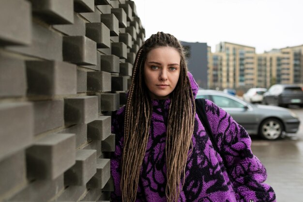 Stylish informal woman with dreadlocks and piercings is dressed in a purple jacket against the