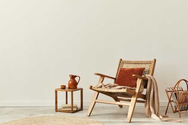 Стильный интерьер гостиной с деревянным креслом, журнальным столиком, мебелью, отделкой из ротанга и элегантными личными аксессуарами. Скопируйте космическую белую стену ..