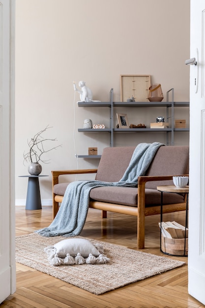 Stylish interior of living room at cozy apartment with brown wooden sofa, coffe table, gray bookstand , pillow, plaid and elegant accessories. Beige and japandi concept. Modern home staging. .