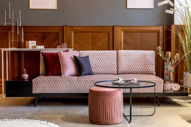 Stylish interior of living room with design pink velvet sofa, elegant pouf, coffee table, plant, pillows, decorations and elegant personal accessories. Modern home decor and home staging..