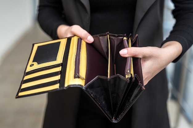 Stylish lady in a black classic suit holds an open empty wallet\
in her gentle hands empty wallet concept