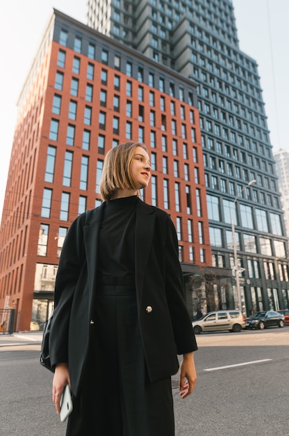 Stylish lady in dark clothing stands against modern architecture