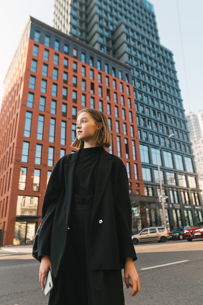 Stylish lady in dark clothing stands against modern architecture