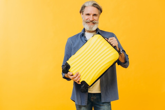 Stylish laughing bearded man holding a yellow suitcase.