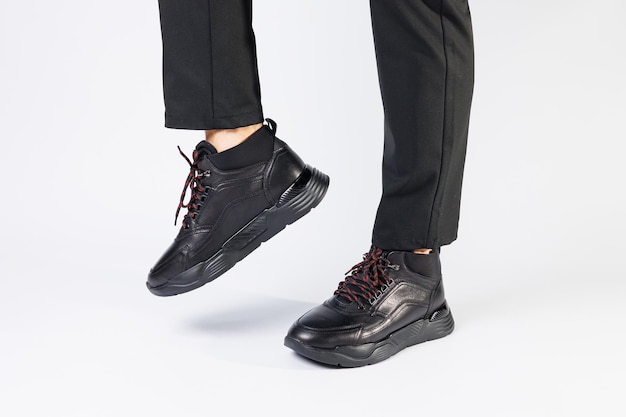 Stylish leather black short men's autumn sneakers on a white background on men's legs. Sneakers winter collection 2022.