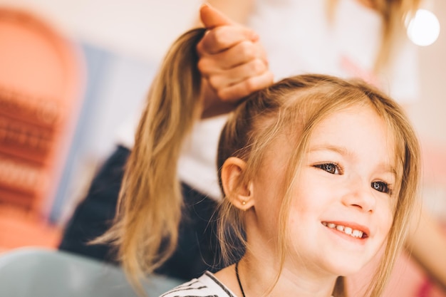 Bambina alla moda in un salone di bellezza per bambini dove ha fatto una bella acconciatura la stilista femminile fa un'acconciatura alla moda per la bambina