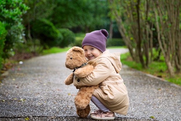 Photo stylish little girl embracing her stuffed teddy bear in autumn park