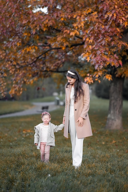 Stylish little girl with mom walks in the park a beautiful girl with her daughter walks in the autum