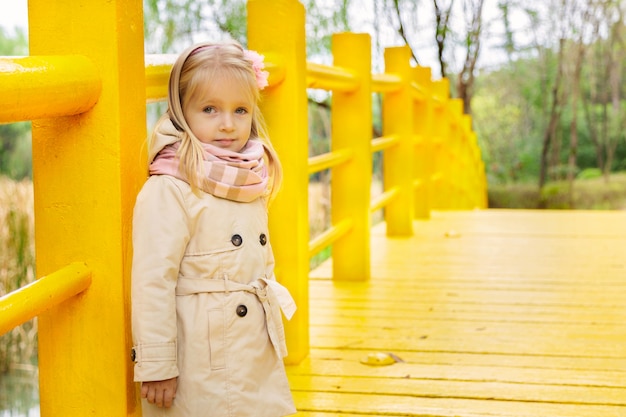 Ragazza alla moda llittle su un ponte giallo nel parco