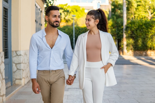 Stylish loving ethnic couple walking together in city