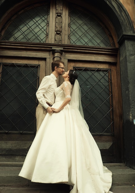Стильная роскошная невеста и элегантный жених нежно обнимаются на фоне старого города Львова