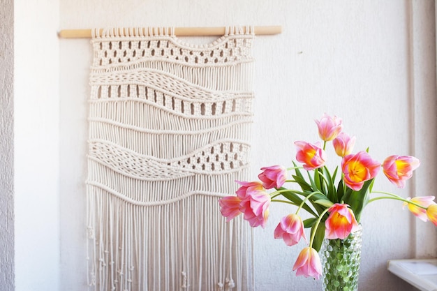 Stylish macrame wall hanging on the white wall above the chest of drawers