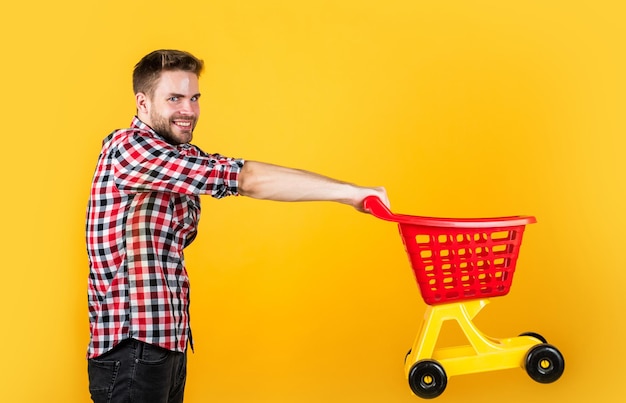 Stylish male carry shopping cart. bearded man in shop store. buy and purchase. prepare for holidays. householding. real shopaholic. young guy in checkered shirt go shopping.