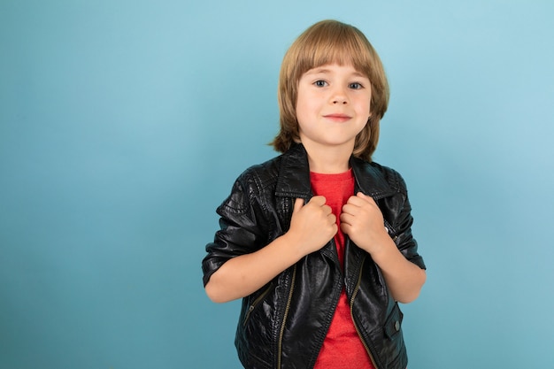 Stylish male child in a leather jacket and a red T-shirt on light blue with copy space