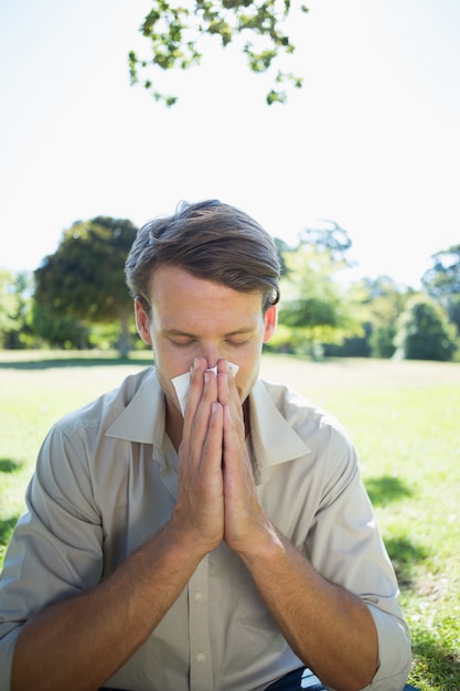 Stylish man blowing his nose in the park