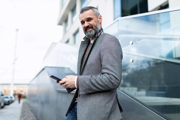 Stylish man in business clothes with a mobile phone in his hands outside