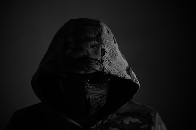 Stylish man in dark hoodie with black glasses and mask dark background hacker attacker and bandit