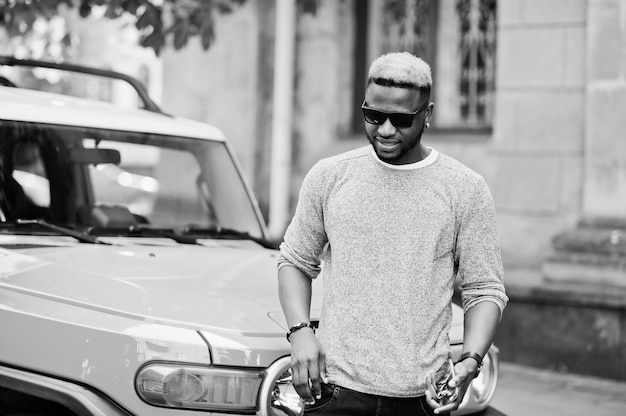 Stylish man on gray sweater and black sunglasses posed on street against yellow car