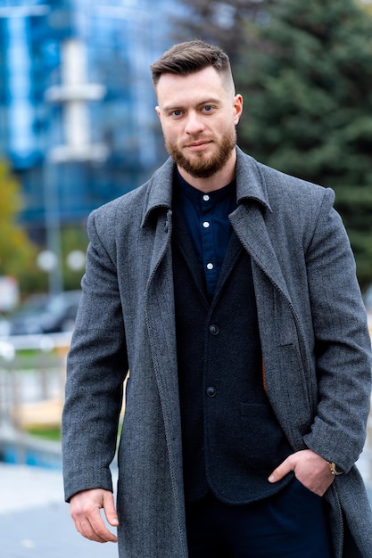 Stylish man holding hand on coat and walking near high buildings Man relaxing walk on modern street Lifestyle concept