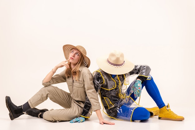 Stylish man in the mask and woman in straw hats posing over white background