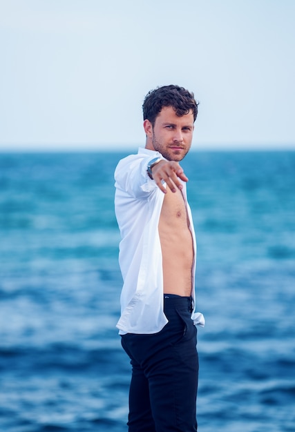 Stylish man reaching out hand on seashore