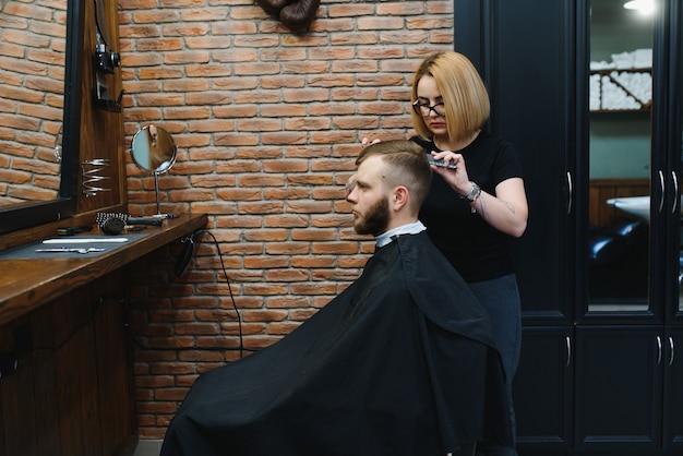 Elegante uomo seduto negozio di barbiere parrucchiere parrucchiere donna che taglia i suoi capelli