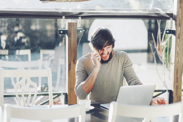 Foto uomo alla moda che si siede in caffè con il computer portatile