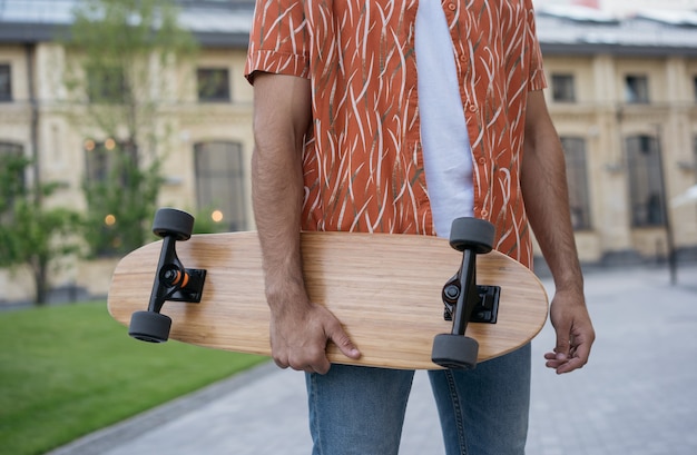 Stylish man skater holding longboard, standing on street