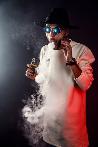 Stylish man in sunglasses puffing the vapor on the black 