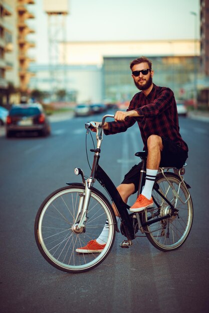 Stylish man in sunglasses riding a bike on city street