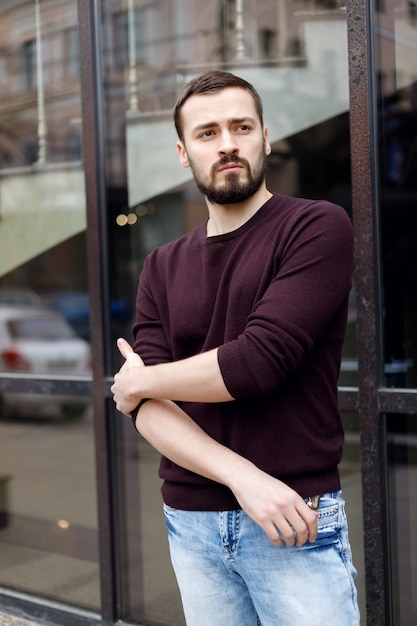 Uomo alla moda con la barba in piedi per strada con un cappotto di pelle. servizio fotografico uomini per strada. un uomo in uno stile alla moda. acconciatura da uomo elegante